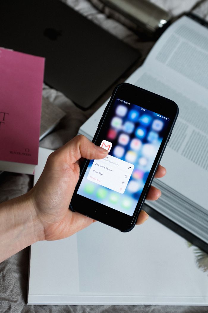 who-we-are Hand holding smartphone with email app open, surrounded by books and laptop.